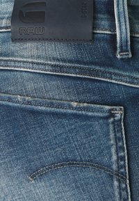Jeans de mezclilla azul oscuro con una etiqueta de cuero con marca en relieve, costuras visibles y un diseño clásico de bolsillos.