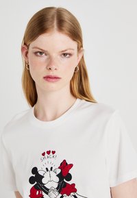 White cotton t-shirt featuring a playful graphic of Mickey and Minnie Mouse in red accents, with the text "SMACK!" above them.