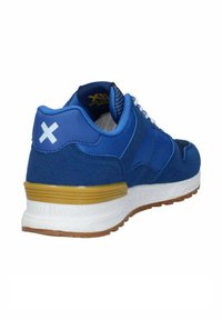 Scarpa sportiva blu con tomaia testurizzata, dettagli bianchi e contrafforte dorato. Include un logo bianco sul retro e una suola resistente.