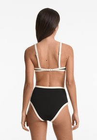 Fekete bikini szett, magas derekú alsókkal, krémfehér részletekkel. A felsőrész vékony, állítható pántokkal és hátul kapcsos záródással rendelkezik.
