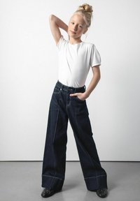 Biała koszulka z krótkim rękawem w połączeniu z ciemnoniebieskimi spodniami o szerokich nogawkach z przednimi kieszeniami i kontrastowym przeszyciem. Całość uzupełniają czarne buty z ćwiekami.