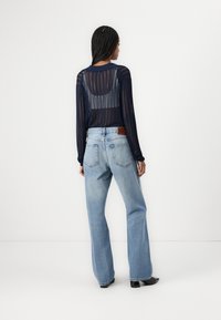 Top de punto transparente de manga larga en color navy, combinado con jeans de pierna ancha de color azul claro, que presentan un patrón texturizado y un cinturón de cuero marrón.