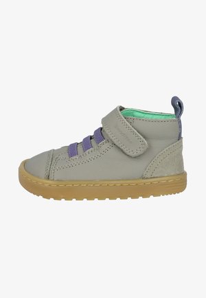 Zapato alto de cuero gris con cordones morados y una correa de velcro. Presenta una suela de goma color canela y un forro interior verde. Materiales lisos y texturizados.