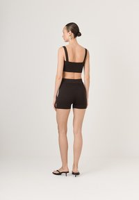 Brązowy prążkowany top w stylu crop z szerokimi ramiączkami i pasującymi szortami o wysokim stanie. Modelka nosi czarne sandały na obcasie, a jej włosy są upięte w kok.
