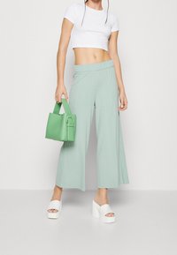 Mintgroene wijde broek met een gestructureerde afwerking, gecombineerd met een wit cropped top, witte platform sandalen en een groene handtas.