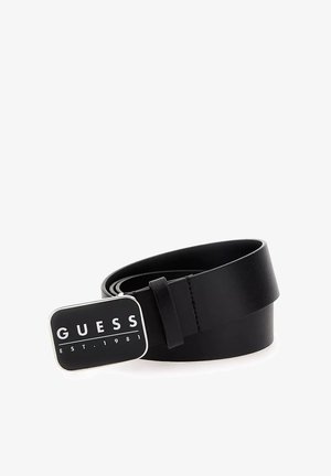 Ceinture en cuir noir avec une boucle rectangulaire en argent portant le logo "GUESS" et le texte "EST. 1981". Texture lisse et design minimal.