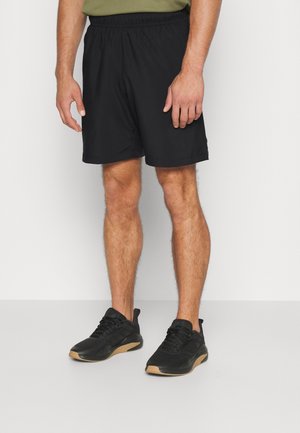 Zwarte, lichte sportshorts met een elastische tailleband, gecombineerd met zwarte sneakers met een rubberkleurige buitenzool. Minimalistisch ontwerp.