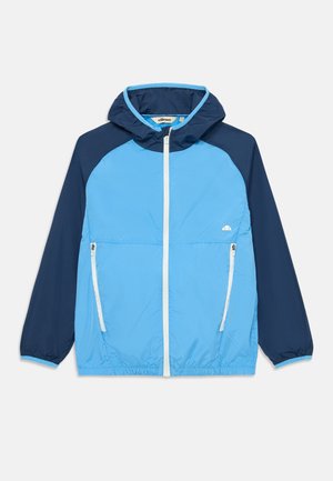 Casaco corta-vento leve azul e marinho com capuz, fecho frontal completo, dois bolsos laterais e punhos elásticos. Apresenta um logótipo no peito.