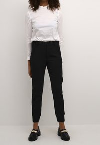 Vit långärmad topp med volangkrage, tillsammans med svarta skräddarsydda byxor. Svarta skor med gulddetaljer. Enkla och rena linjer.