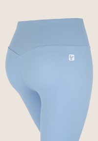Leggings blu a vita alta realizzati in tessuto elasticizzato, con superficie liscia, cuciture piatte e un piccolo logo sul retro in basso.