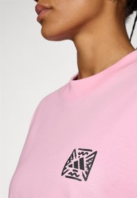 Tricou cu mânecă scurtă, roz, dintr-un amestec de bumbac. Are un logo grafic negru pe piept. Textură netedă și decolteu rotund.