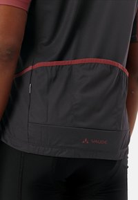 Maillot de sport noir avec accents bordeaux, comportant des panneaux en mesh, un logo à l'ourlet et une coupe ajustée pour la performance.