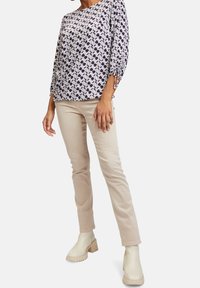 Leichtes, gemustertes Blusenshirt mit Dreiviertelärmeln und Kordelzug-Akzenten, kombiniert mit beigen, figurschmeichelnden Hosen und beigen Stiefeletten.