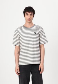 T-shirt a righe grigio e bianco con maniche corte, collo rotondo e un piccolo ricamo floreale nero sul petto.