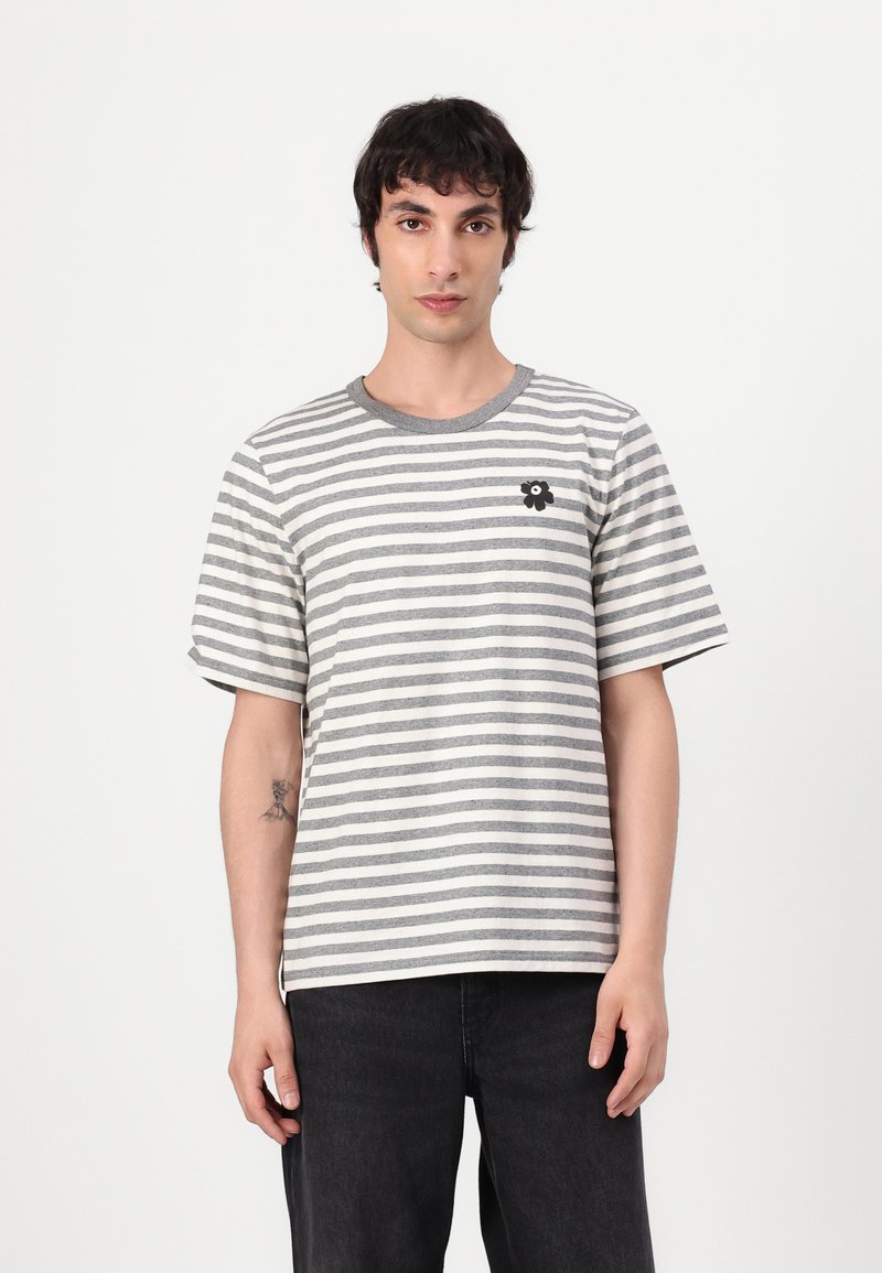 T-shirt a righe grigio e bianco con maniche corte, collo rotondo e un piccolo ricamo floreale nero sul petto.