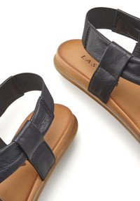 Schwarze Sandalen mit zwei breiten Riemen, Obermaterial aus strukturiertem Kunstleder und einem gepolsterten Fußbett in Beige. Elastisches Band für einen sicheren Sitz. Flache Sohle.