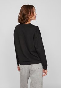 Felpa nera con scollatura rotonda e spalle basse. Tessuto morbido. Abbinata a jeans alta vita grigi chiari.