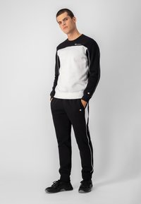 Chándal en blanco y negro que consiste en un sudadera de cuello redondo con un frente blanco sólido y mangas negras, combinado con pantalones negros con franjas laterales blancas.