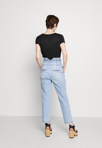 Světle modré džíny s vysokým pasem a volným střihem, s dvěma zadními kapsami a V-švem na zadním sedle. V kombinaci s černým tričkem.