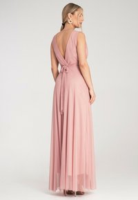 Długa, zwiewna różowa sukienka z głębokim dekoltem z tyłu, krótkimi rękawami i zawiązanym w pasie. Wykonana z lekkiego materiału o gładkiej fakturze.
