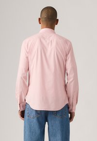 Camisa de manga larga rosa claro con cuello estándar, dobladillo recto y puños abotonados, combinada con vaqueros de denim azul.