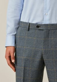 Blue and gray plaid trousers with a textured fabric, featuring yellow accents, a single button closure, and side pockets.