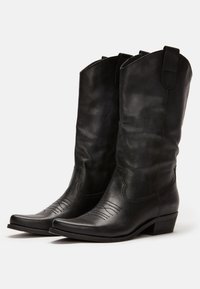 Czarne kowbojskie buty ze skóry z szpiczastym noskiem, dekoracyjnym przeszyciem na cholewce i niskim, warstwowym obcasem. Charakterystyczne dla klasycznego stylu westernowego.