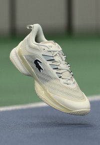 Světle béžová sportovní obuv s texturovaným svrškem, syntetickými materiály, černým logem a hladkou podrážkou. Omezené akcentové barvy.