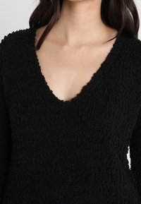 Pull noir en tissu texturé et pelucheux avec un décolleté en V profond. Le design inclut des manches longues et une coupe ample.
