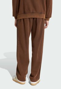 Brauner Sweatshirt und passende Hose aus weichem Stoff, mit lockerer Passform, sichtbaren Nähten und leichten seitlichen Streifen.