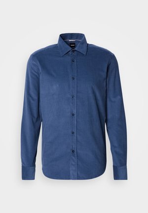 Camicia da uomo a maniche lunghe in tessuto di velluto a coste blu, con colletto a punta e bottoni neri visibili lungo la parte anteriore.