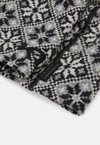 Svart och grå mönstrad textil med intrikata geometriska mönster; mjukt stickat material med en synlig etikett och kontrasterande sömmar.