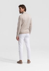 Licht beige gebreide trui met een hoge kraag, gedragen met witte slim fit broek en grijze instap schoenen, gezien van achteren.