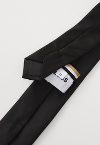 Gravata de seda preta com uma textura suave, apresentando uma ponta afilada. Etiqueta visível com o tamanho "T2" e nome da marca. Design simples e elegante.