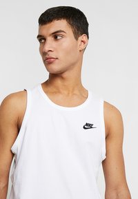 Fehér ujjatlan pamut trikó, kerek nyakkivágással, bal mellkas tájékán egy kis fekete Nike logóval.