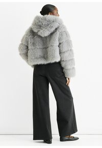 Gray fur cropped jacket with a hood, featuring a textured, plush finish and boxy design. Paired with wide-leg black jeans and flat shoes.