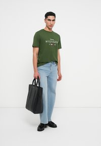 Zelené bavlněné tričko s bílým logem "Tommy HILFIGER", spárované se světle modrými džíny a strukturovanou černou kabelkou. Černé boty dokončují vzhled.