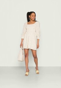 Vestido de manga curta com estampado floral em creme claro e decote quadrado. Silhueta fluida, combinado com sandálias de bloco amarelas e uma bolsa tote.
