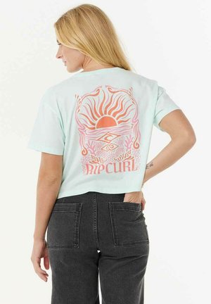 T-shirt cropped vert menthe avec un graphique de soleil et de vagues en rose et orange, avec le texte "RIP CURL" en dessous du design.