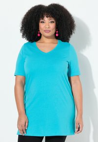 Un T-shirt turquoise à col en V avec des manches courtes, doté d'une coupe loose et d'un tissu doux et lisse. L'ourlet inférieur est légèrement courbé.