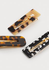 Set of three hair clips in tortoiseshell patterns. Colors include amber, black, white, and gold accents. Rectangular shape, glossy finish.