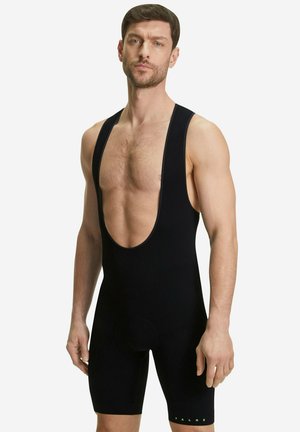 Black cycling bib short with wide shoulder straps, ribbed texture, a low-cut front, and a subtle brand logo in green at the hem.