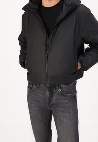 Schwarze Kapuzenjacke mit Reißverschluss und elastischen Bündchen, kombiniert mit dunkelgrauen Jeans im klassischen Fünf-Taschen-Design. Minimalistischer Stil.