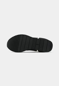 Black shoe sole with textured rubber, featuring horizontal grooves and a patterned tread. The design shows durability and traction.