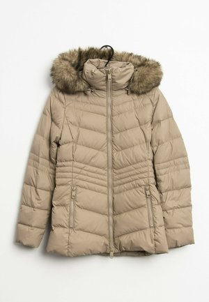 Veste d’hiver matelassée beige avec fermeture éclair devant, deux poches zippées et une capuche bordée de fourrure suspendue à un cintre noir.