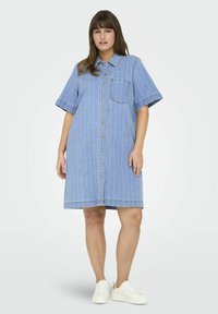 Jeansklänning med korta ärmar, blå och vita vertikala ränder, framknäppning och bröstficka. Bärs med vita sneakers.