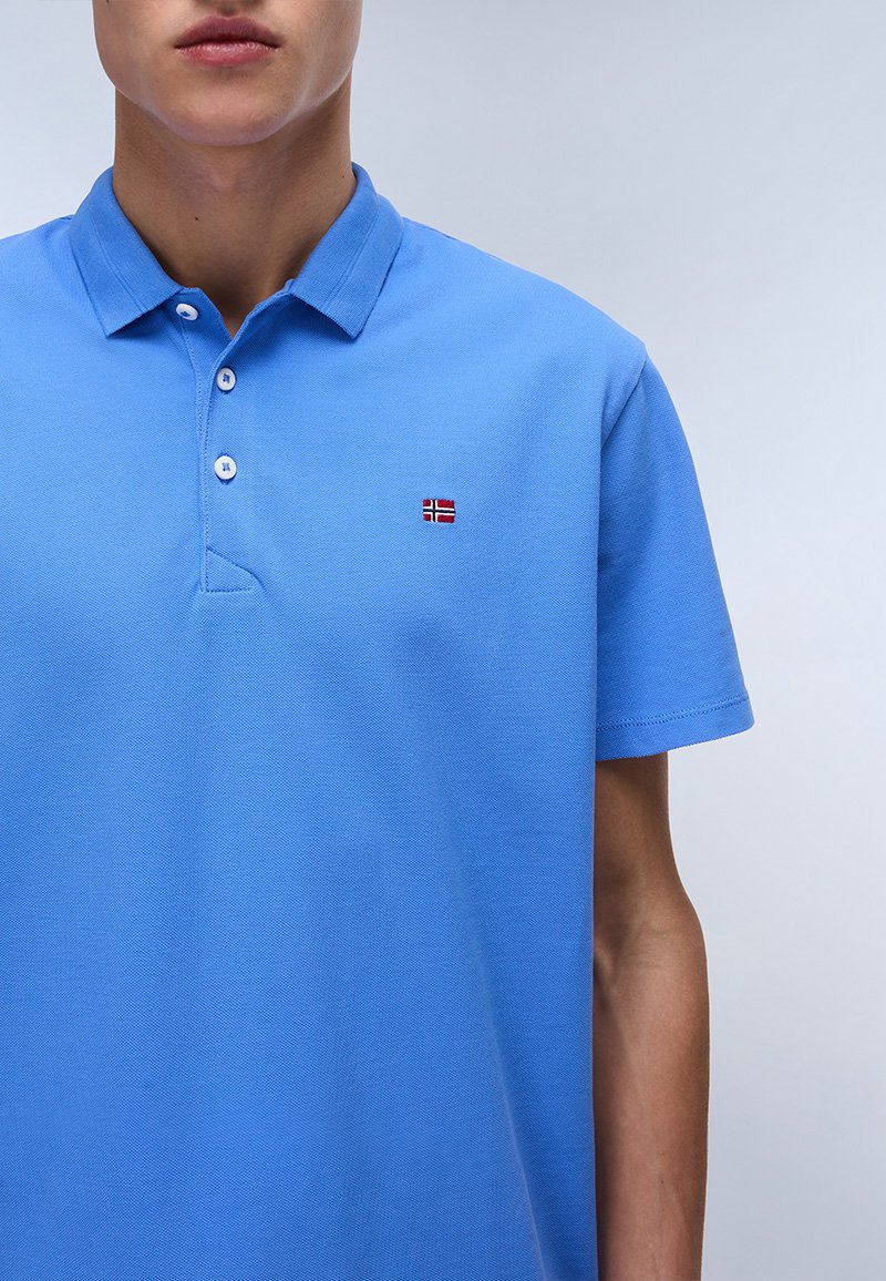 Polo en coton bleu clair avec un col classique, des manches courtes et un petit drapeau norvégien brodé sur la poitrine gauche.