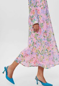 Robe longue à manches longues à fleurs roses, avec des motifs de feuilles vertes et multicolores. Complétée par des escarpins bleu à bout pointu.