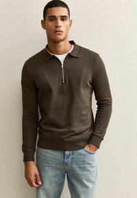 Felpa zip-up marrone con colletto, maniche lunghe e polsini a coste, abbinata a jeans di denim blu chiaro. Texture liscia e vestibilità casual.