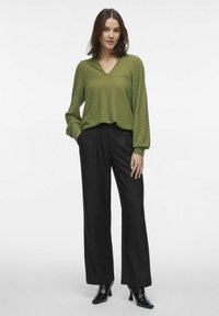 Grøn zigzag-mønstrede blouse med v-hals og lange ærmer, parret med højtaljede sorte brede bukser og spidse sorte stiletter.